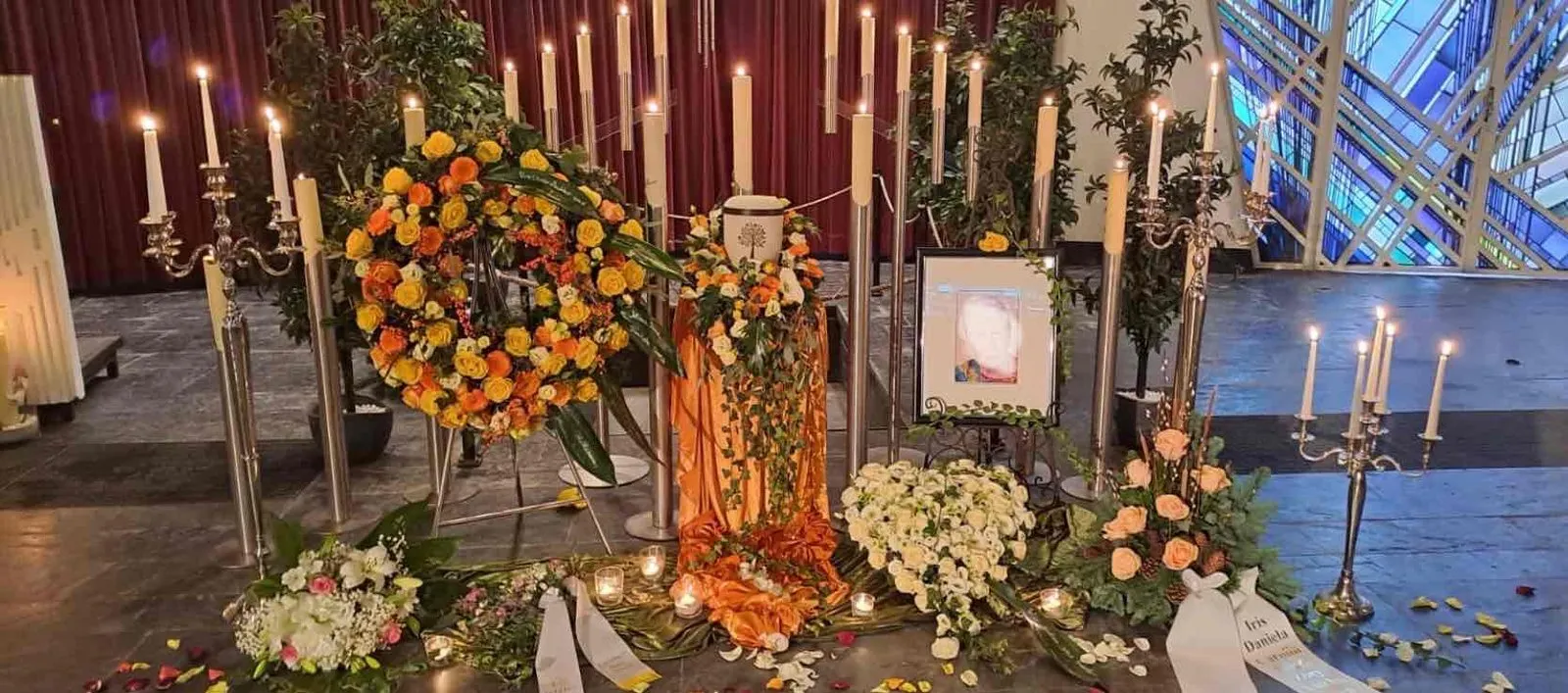 Gesamtansicht einer Trauerfeier-Dekoration mit orangen und gelben Blumenkränzen