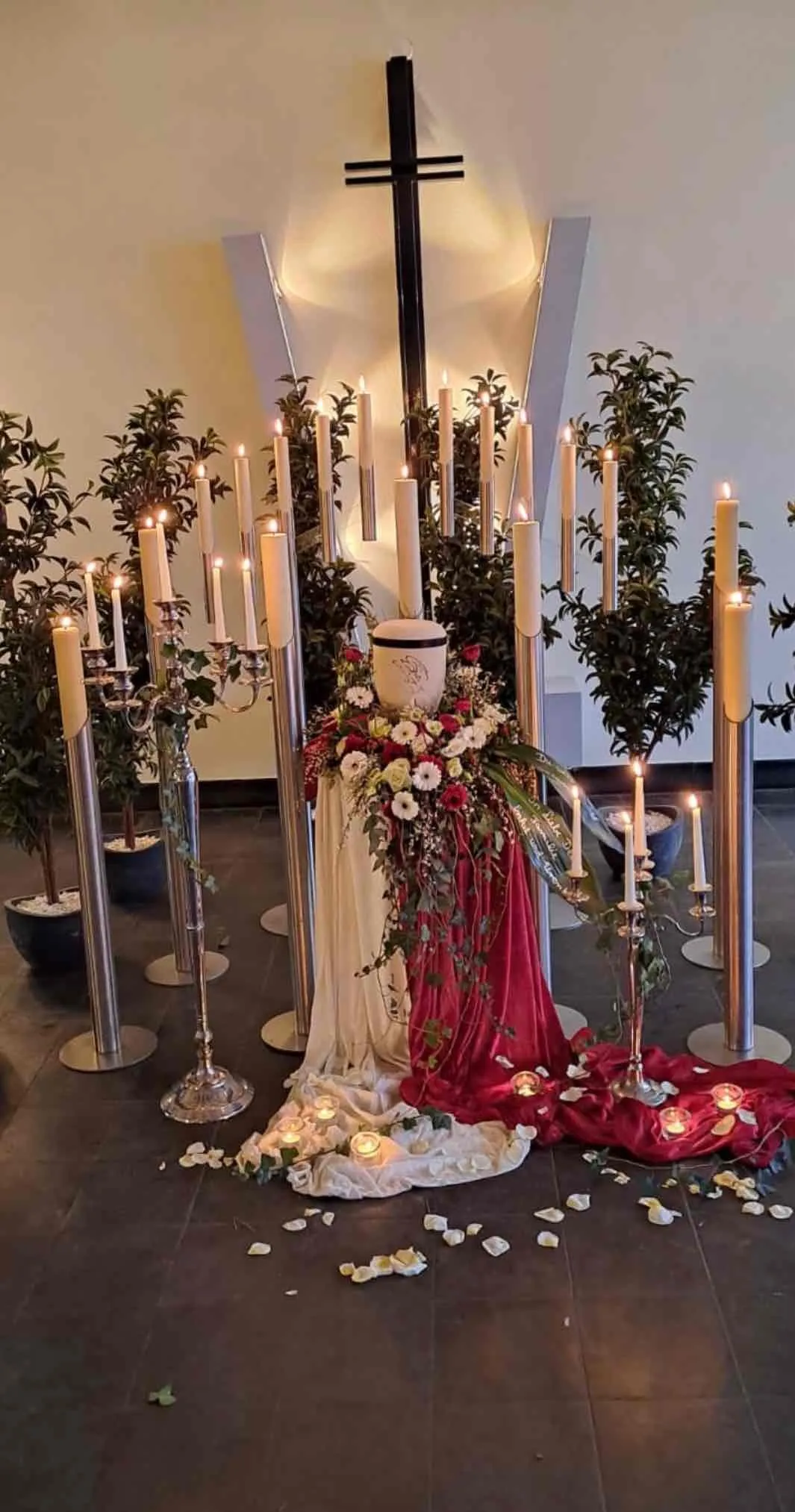 Urnenschmuck mit roten und weißen Blumen, umgeben von Kerzen